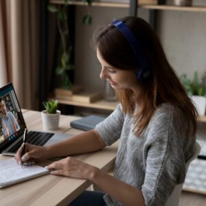 Woman video calling on laptop with headphones at home desk.