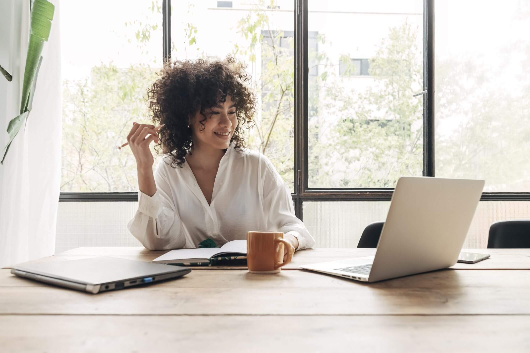 A woman working thoughtfully at a desk with a laptop and coffee.